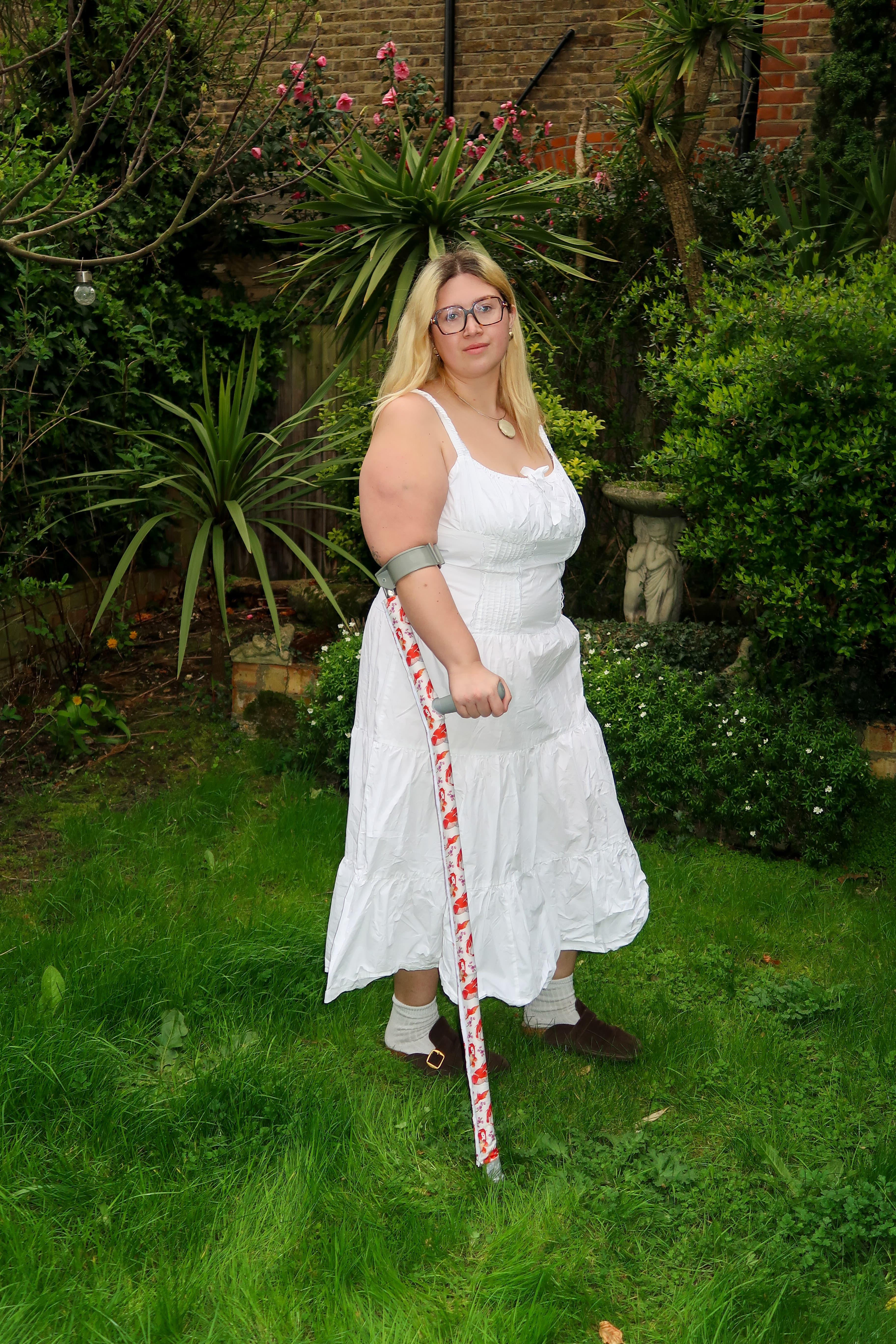 Aisha wearing a white dress using crutches with a Strydr floral cover outdoors
